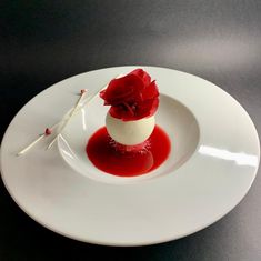 a white plate topped with a dessert covered in red sauce and a single rose on top