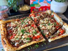 a pizza with various toppings sitting on top of a wooden cutting board next to a box of cereal