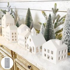 a christmas scene with white houses and evergreen trees on a mantel in front of a wood paneled wall