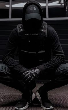 a man sitting on the ground in front of a building wearing a hoodie and gloves