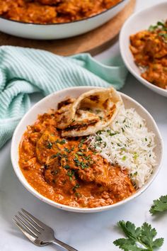 two bowls filled with curry and rice on top of a white table next to silverware