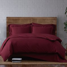 a bed with red sheets and pillows on top of it next to a plant in a vase