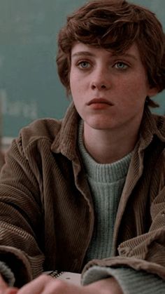 a young boy sitting at a desk with his hand on the keyboard and looking off into the distance