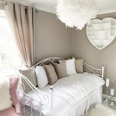 a white day bed sitting in a bedroom next to a window with a heart shaped mirror on the wall