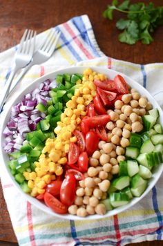 a white bowl filled with vegetables on top of a table next to a fork and knife