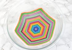 a glass bowl filled with multicolored crochet coasters on top of a marble counter