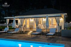 an outdoor pool and gazebo at night with lights on the patio, chairs and tables