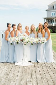 a group of women standing next to each other on a wooden dock holding bouquets