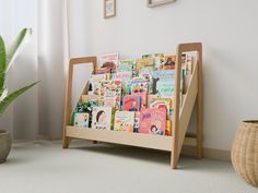 a wooden magazine rack with books on it next to a potted plant and window