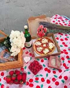 a table topped with pizza and flowers next to bottles of wine on top of a blanket