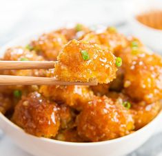 a white bowl filled with meatballs covered in sauce and green onions, with two wooden chopsticks sticking out of it