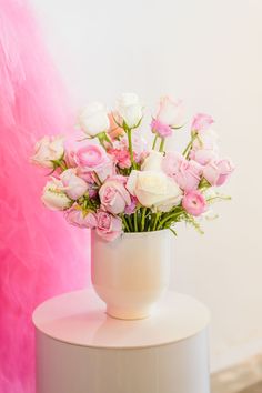 a white vase filled with pink and white flowers on top of a table next to a pink wall