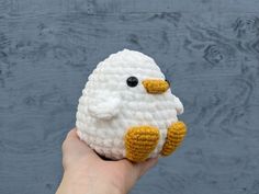 a hand holding a small crocheted white and yellow bird with black eyes on it's face