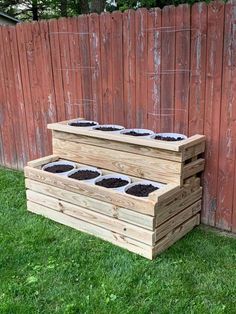 a wooden planter filled with dirt in front of a red fence and green grass