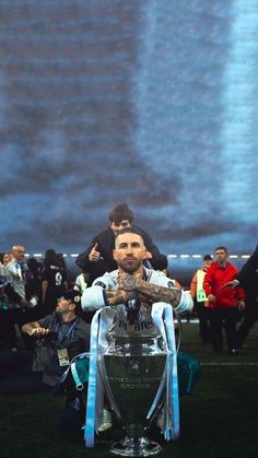 a man sitting on top of a soccer trophy in front of a large group of people