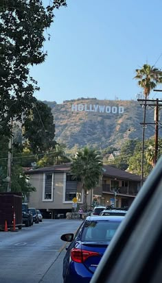 the hollywood sign is in the distance behind cars parked on the side of the road