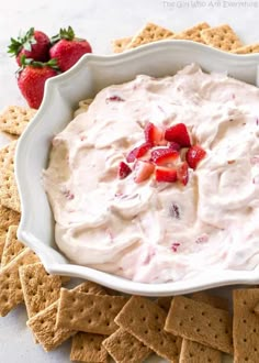 a white bowl filled with fruit dip surrounded by crackers and strawberries on the side