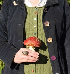 a woman holding a mushroom with buttons on it's back and wearing a green sweater