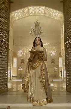 a woman dressed in an elaborately designed dress and holding a chandelier is standing in the middle of a hall