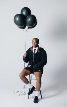 a woman sitting on a chair holding black balloons