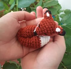 a small crocheted animal is being held in someone's hand with green leaves behind it