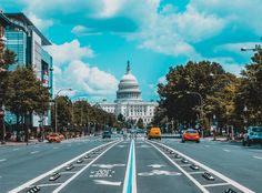 the capitol building is in the background as cars drive down an empty street with blue lines painted on it