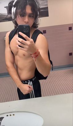 a shirtless man taking a selfie in front of a mirror with headphones on