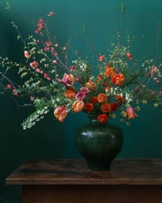 a vase filled with lots of flowers on top of a wooden table next to a green wall