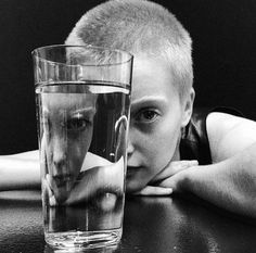 a black and white photo of a man leaning his head on a table next to a glass of water