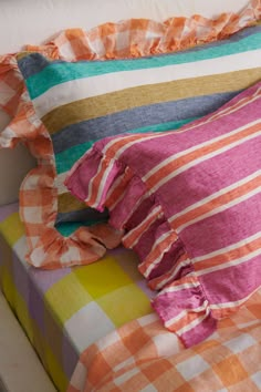 an orange and pink striped pillow sitting on top of a colorful bed cover with ruffled edges