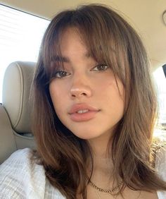 a woman sitting in the back seat of a car wearing a white shirt and gold necklace