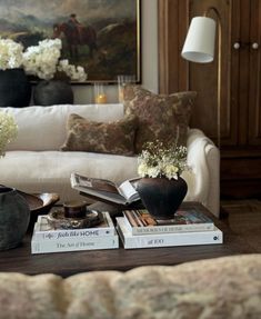 a living room filled with furniture and lots of books on top of each other in front of a painting