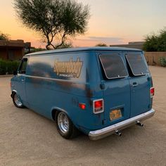 an old blue van parked in a parking lot with the sun setting on it's horizon