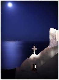 a cross on the side of a building with water in the background at night time