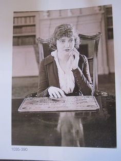 an old photo of a woman sitting at a table with a book in front of her