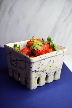 a white bowl filled with strawberries on top of a blue table