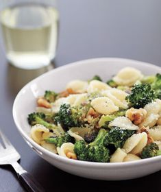 a white bowl filled with pasta and broccoli next to a glass of water