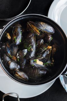 a pan filled with mussels sitting on top of a table next to plates