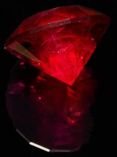 a bright red diamond sitting on top of a table next to a black background with reflections