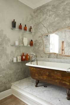 a bath tub sitting under a bathroom mirror next to a shelf with bottles on it