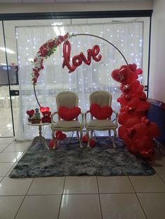 two chairs are set up in front of a valentine's day love arch with red balloons