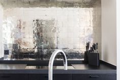 a kitchen counter with a sink and faucet in front of a tiled wall