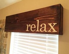 a wooden sign that says relax hanging on the wall next to a window with shutters