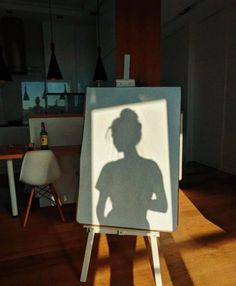 a shadow of a woman is on an easel in the middle of a room