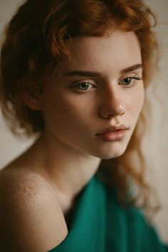 a woman with freckled hair and blue eyes is looking at the camera while wearing a green dress