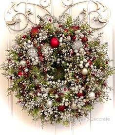 a christmas wreath hanging on the front door with ornaments and greenery in silver, red and white