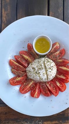 a white plate topped with sliced tomatoes and cheese next to a small bowl of dipping sauce