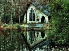 an old church sits in the middle of a forest next to a body of water