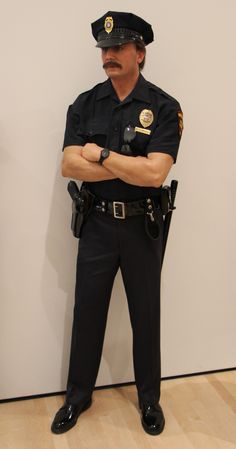 a police officer standing in front of a white wall with his arms crossed and looking at the camera