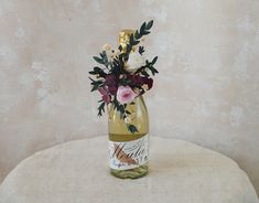 a wine bottle with flowers in it sitting on a tablecloth covered stool next to a wall